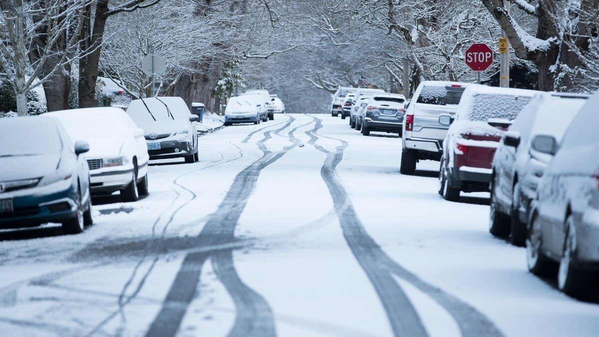 snowy and icy street with parked cars covered in thin layer of snow