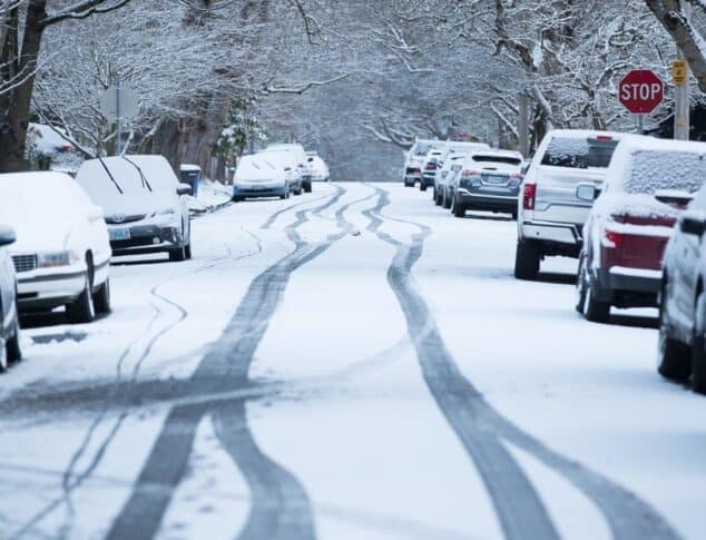 snowy and icy street with parked cars covered in thin layer of snow