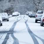 snowy and icy street with parked cars covered in thin layer of snow