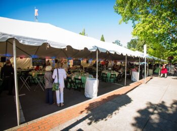 Tented venue space with pink and green tables and guests underneath on a sunny day in Forest Grove