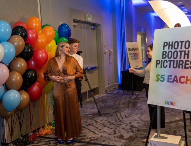 A couple posing in front of many colorful balloons for a photo booth picture at Q Center's SHINE event