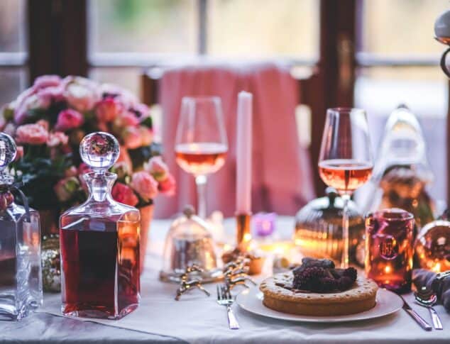 Beautiful table setting with pastry and carafe in focus, pink flowers and ambient light in background