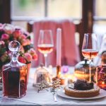 Beautiful table setting with pastry and carafe in focus, pink flowers and ambient light in background
