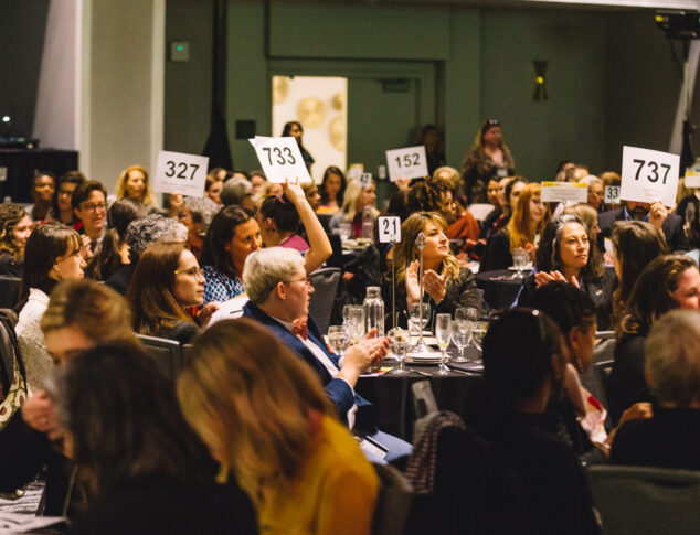 People at Center for Women's Leadership luncheon sitting around tables with some bid paddles raised in the air
