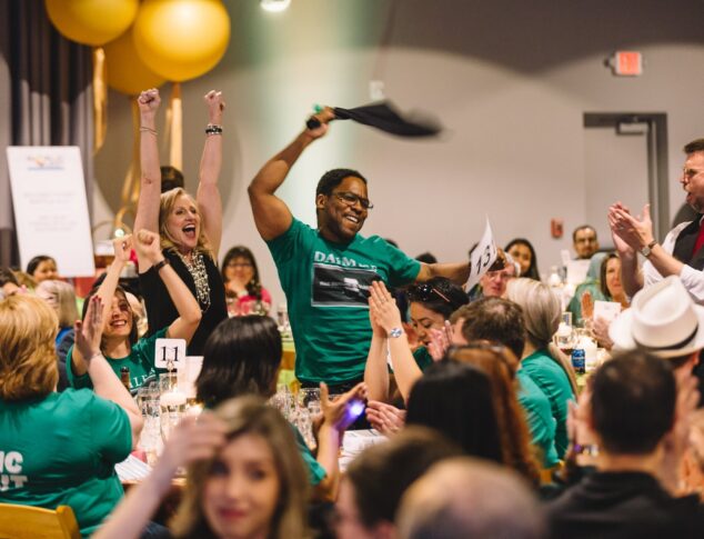 Man celebrating while surrounded by cheering teammates at WorldOregon's fundraising gala