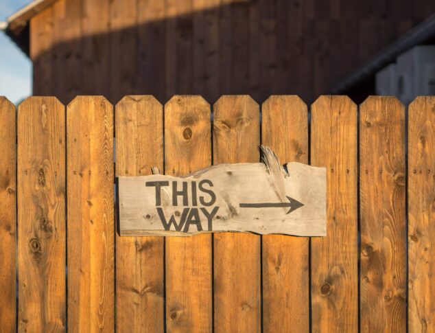 Wooden sign reading THIS WAY affixed onto wooden fence