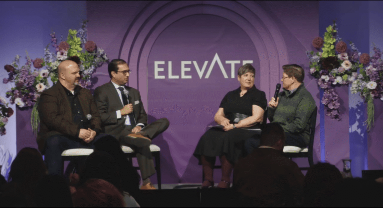 Four speakers seated on a stage with microphones against a purple backdrop with the word Elevate printed in large letters